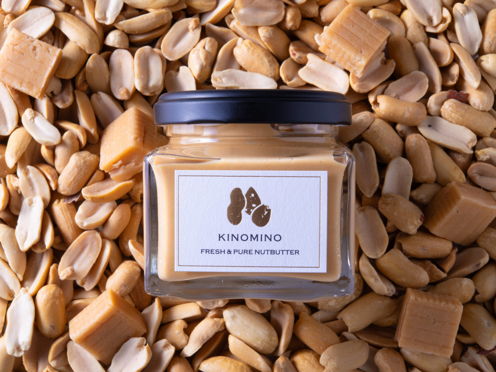 沢山のピーナッツとキャラメルを背景にした、塩キャラメルピーナッツバターの商品写真